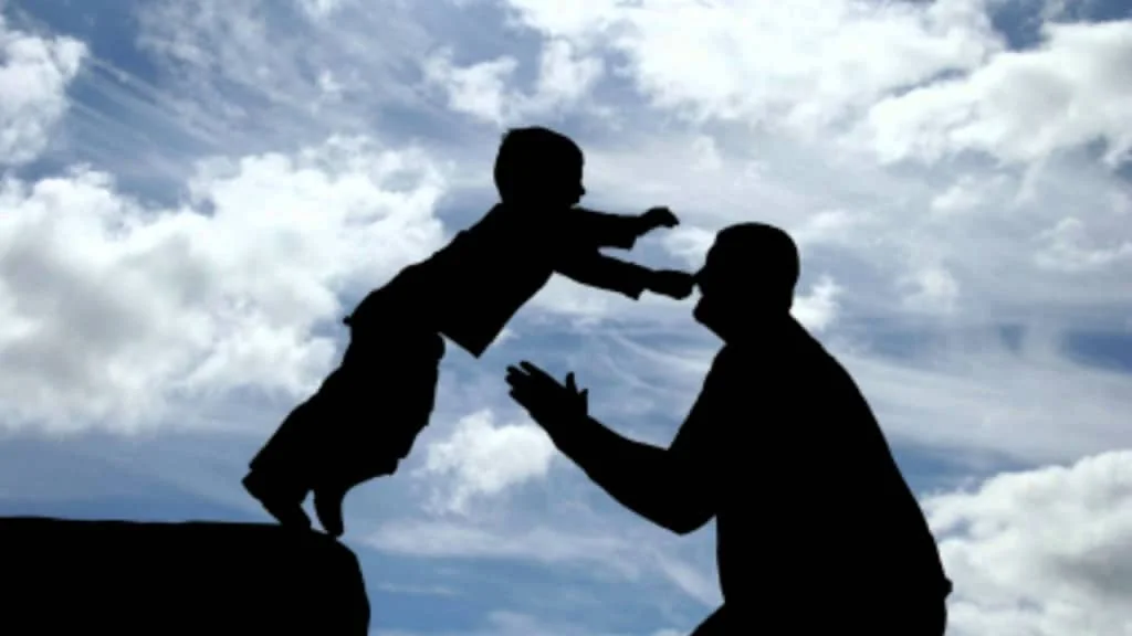 Silhouette of a child leaping from a ledge into an adult's waiting arms against a cloudy sky