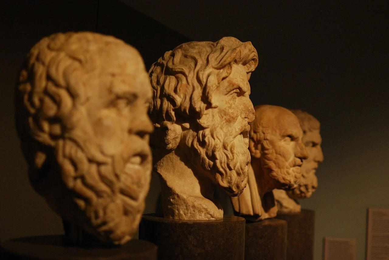 Row of ancient marble busts of bearded philosophers on pedestals in a dim museum