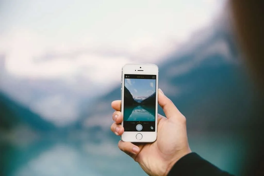 Hand holding a smartphone taking a photo of a mountain lake